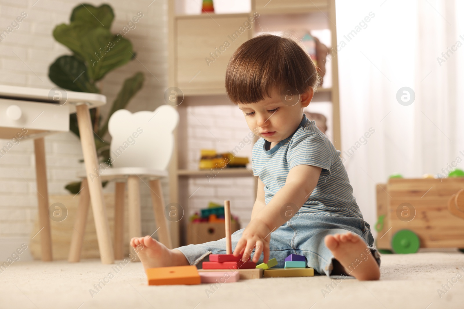 Photo of Cute little boy playing with toy pyramid on floor at home, space for text