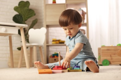 Photo of Cute little boy playing with toy pyramid on floor at home, space for text