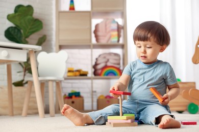 Photo of Cute little boy playing with toy pyramid on floor at home, space for text