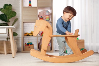 Photo of Cute little boy near wooden rocking horse at home