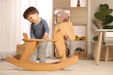 Photo of Cute little boy near wooden rocking horse at home