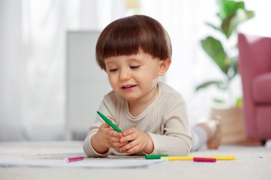 Photo of Cute little boy drawing on floor at home