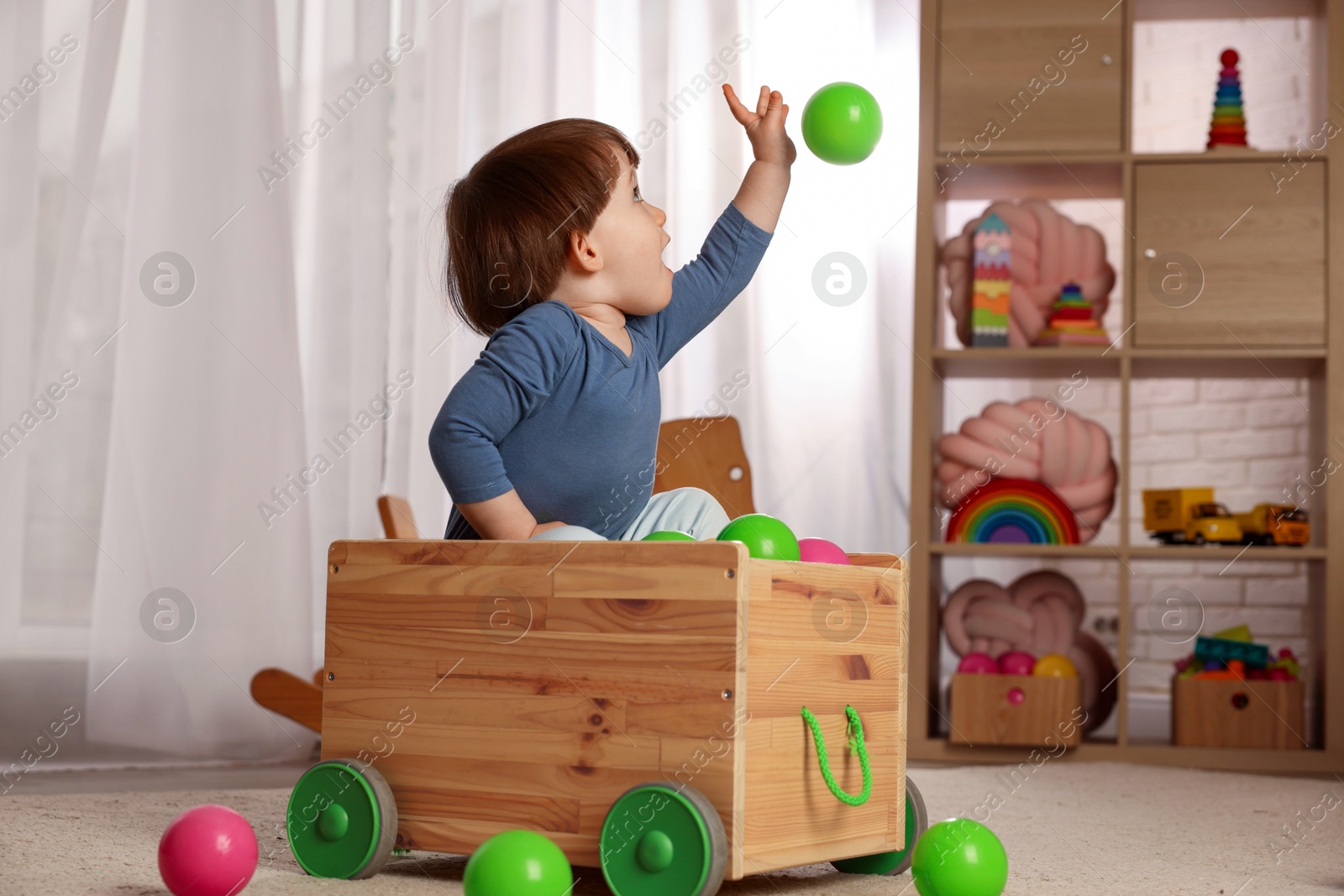 Photo of Cute little boy playing in wooden cart at home