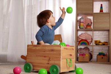 Photo of Cute little boy playing in wooden cart at home