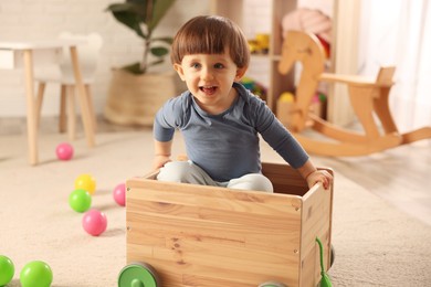 Photo of Cute little boy playing in wooden cart at home