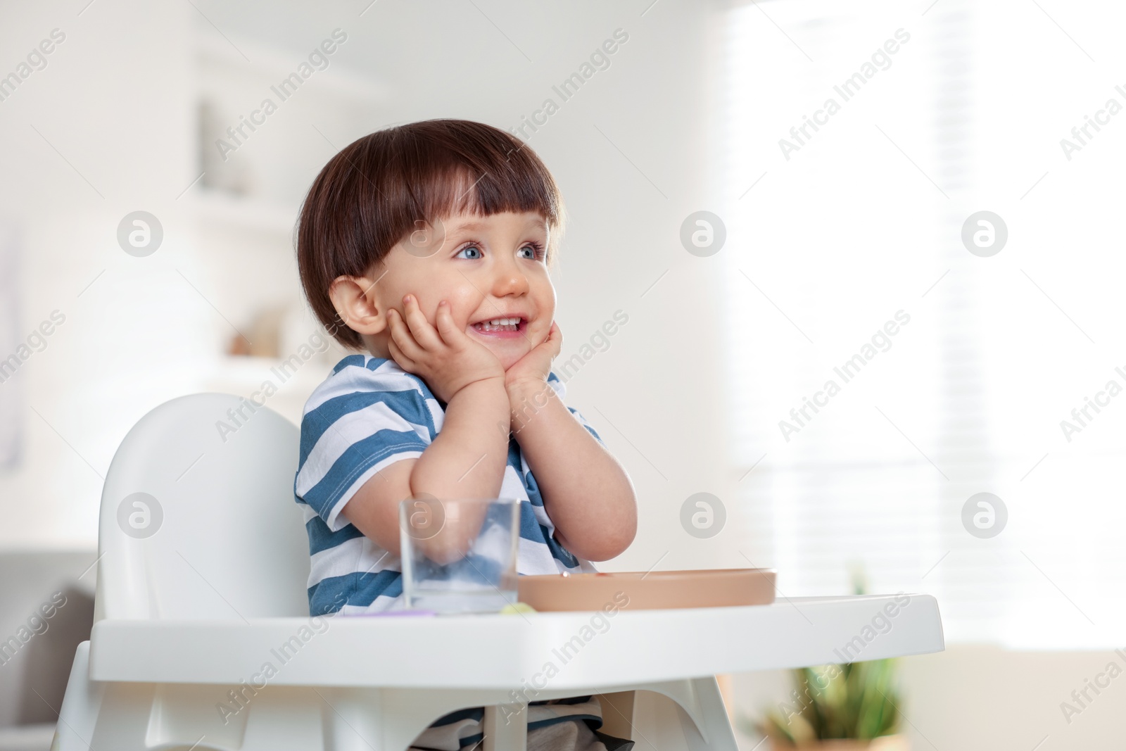 Photo of Cute little boy sitting in high chair at home