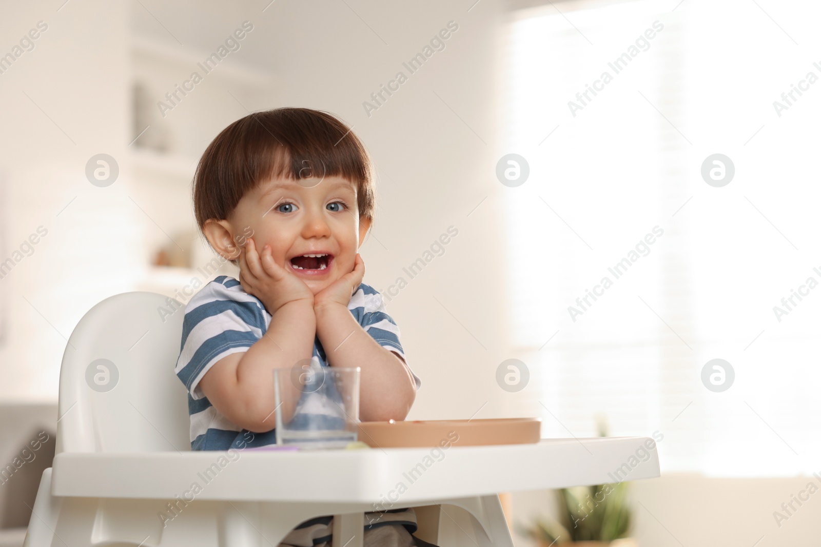 Photo of Cute little boy sitting in high chair at home