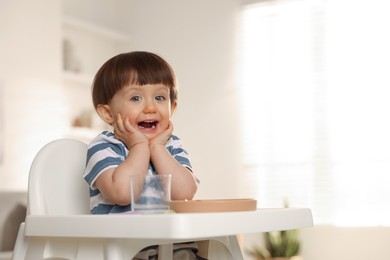 Photo of Cute little boy sitting in high chair at home