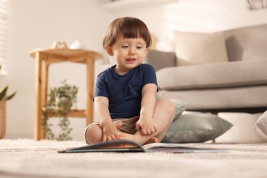 Photo of Cute little boy with book on floor at home