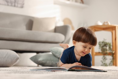 Photo of Cute little boy with book on floor at home, space for text