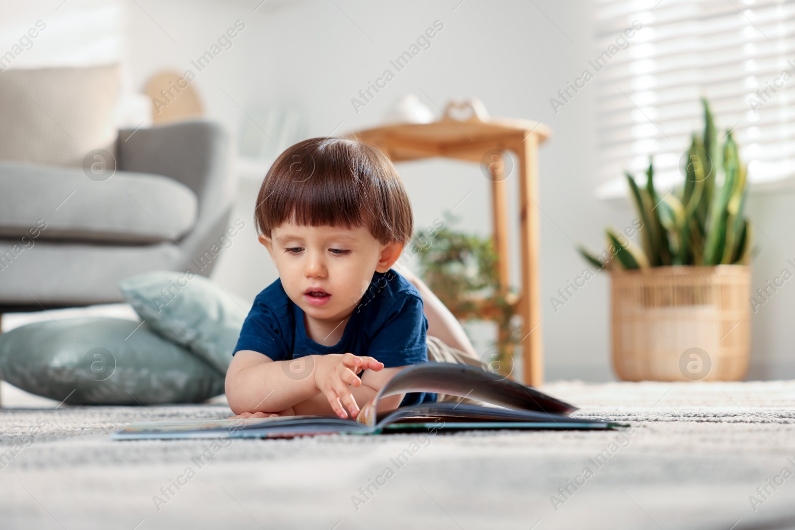 Photo of Cute little boy with book on floor at home