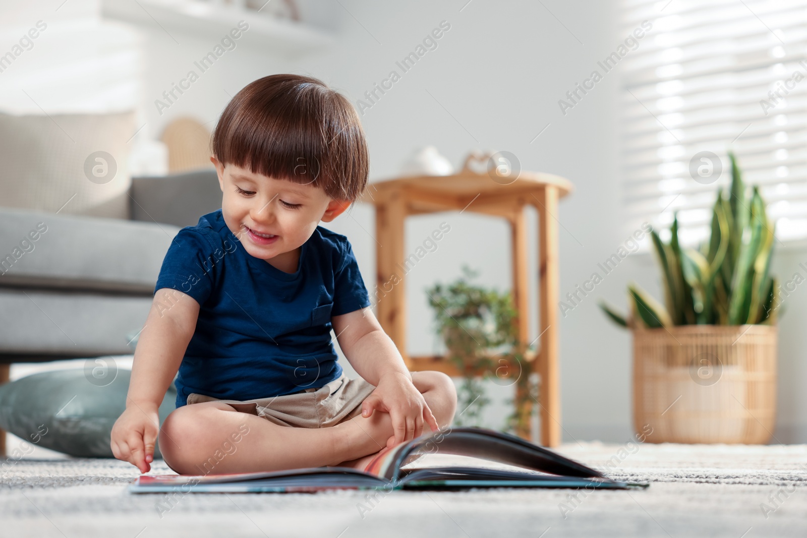 Photo of Cute little boy with book on floor at home, space for text