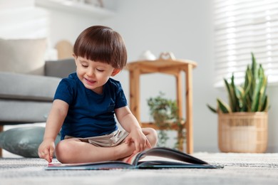 Photo of Cute little boy with book on floor at home, space for text