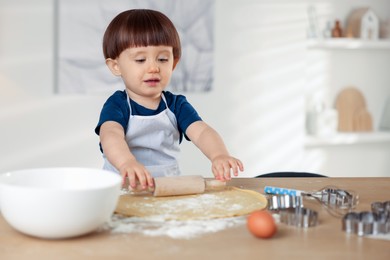 Photo of Cute little boy shaping dough with rolling pin at table indoors