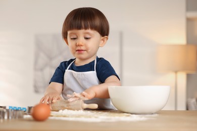 Photo of Cute little boy shaping dough with rolling pin at table indoors