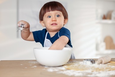 Photo of Cute little boy making dough at table indoors