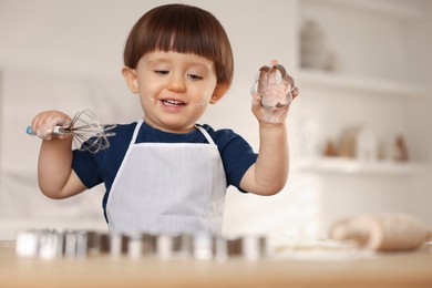 Photo of Cute little boy with cookie cutter and whisk at table indoors, space for text