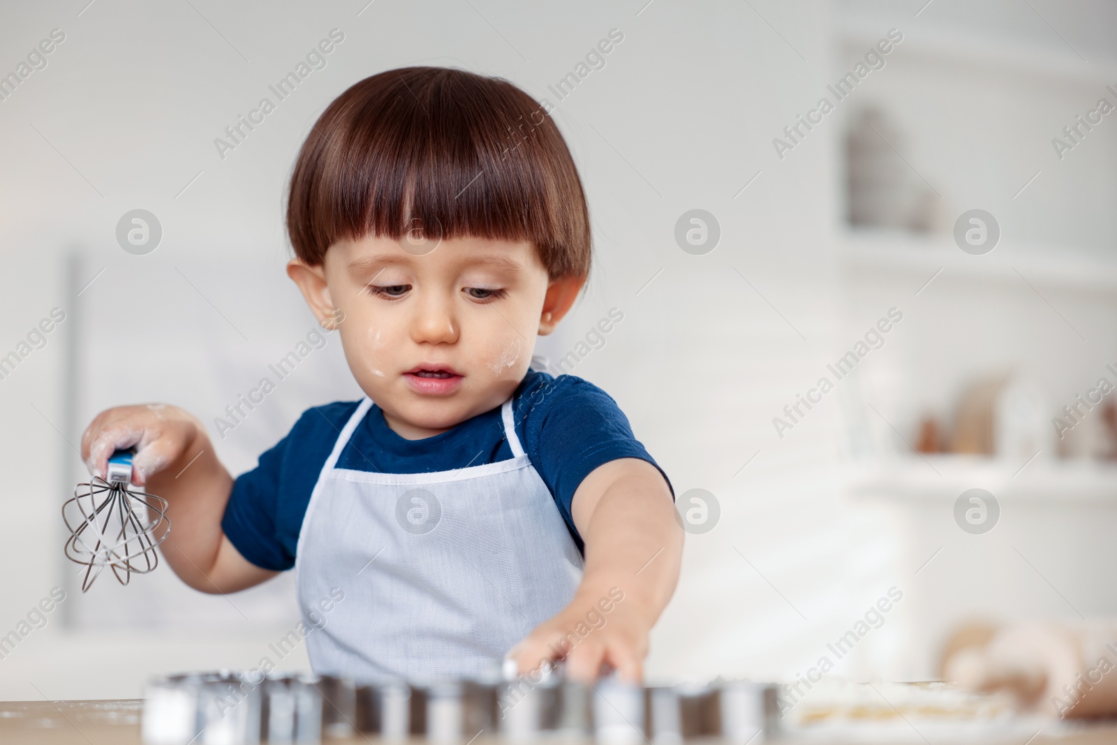 Photo of Cute little boy with whisk at table indoors, space for text