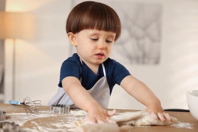 Photo of Cute little boy kneading dough at wooden table indoors