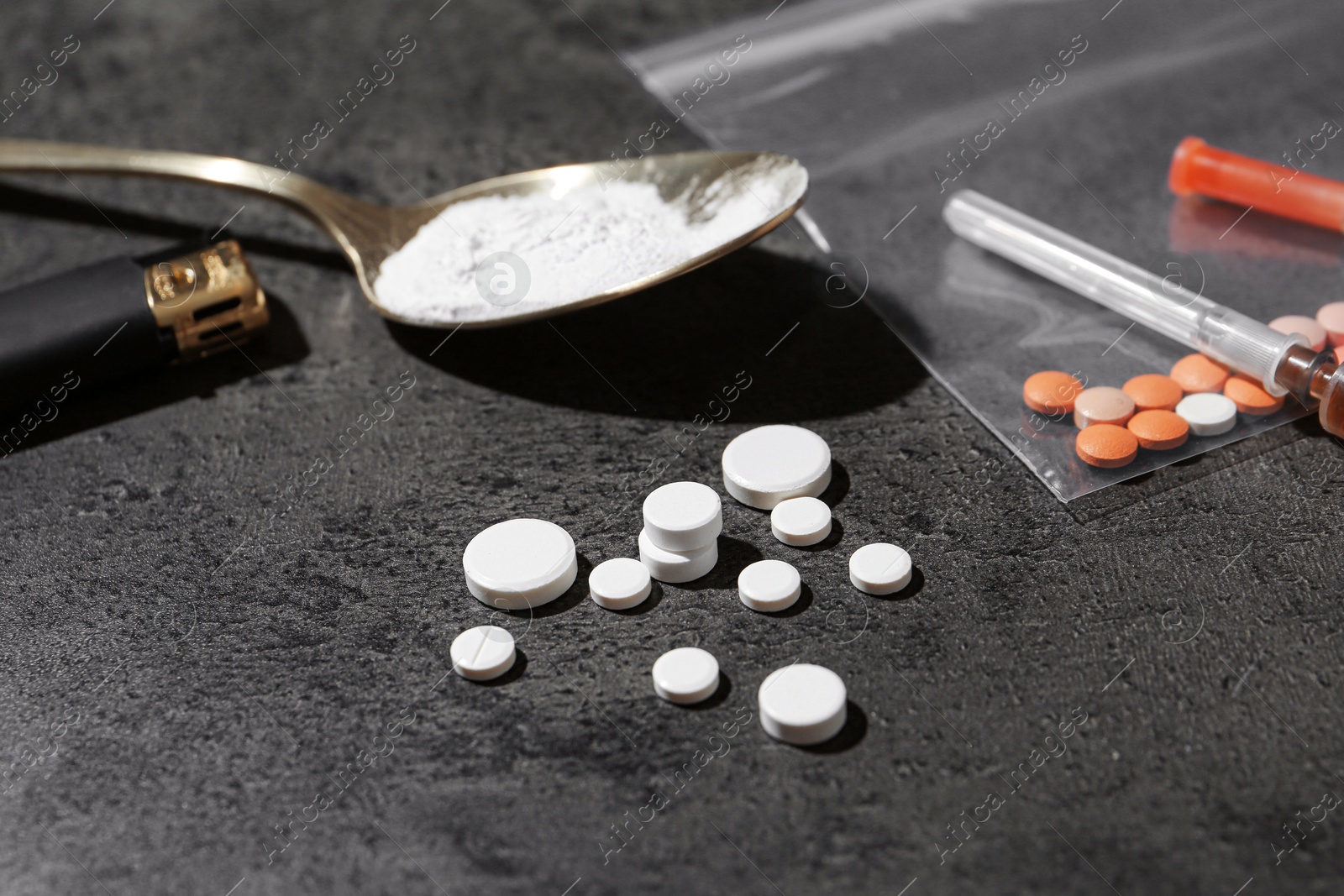 Photo of Drug addiction. Spoon with powder, pills, cigarette lighter and syringe on gray textured table, closeup