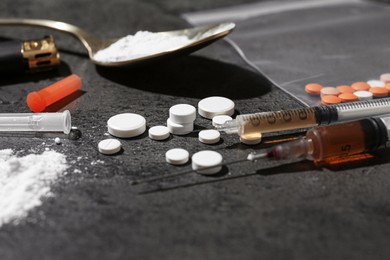 Photo of Drug addiction. Pills, syringes and spoon with powder on gray textured table, closeup