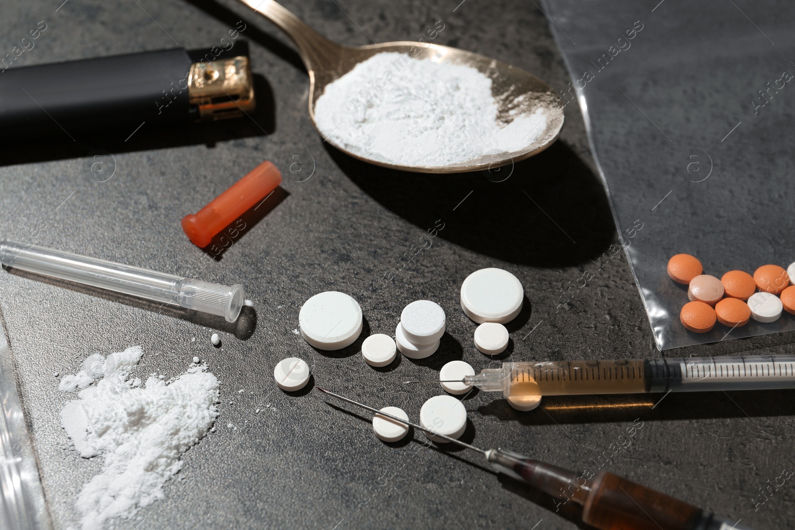 Photo of Drug addiction. Spoon with powder, pills, syringes and cigarette lighter on gray textured table, closeup