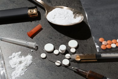 Photo of Drug addiction. Spoon with powder, pills, syringes and cigarette lighter on gray textured table, closeup