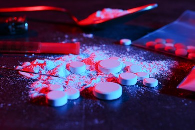 Photo of Drug addiction. Pills, powder and syringe on dark table in neon lights, closeup