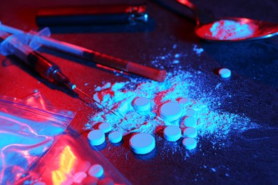 Photo of Drug addiction. Powder, pills and syringes on dark table in neon lights, closeup