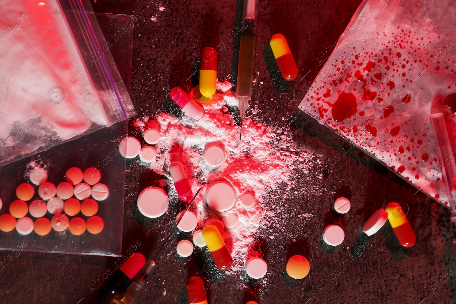 Photo of Drug addiction. Different pills, powder and syringes on dark textured table in color light, flat lay