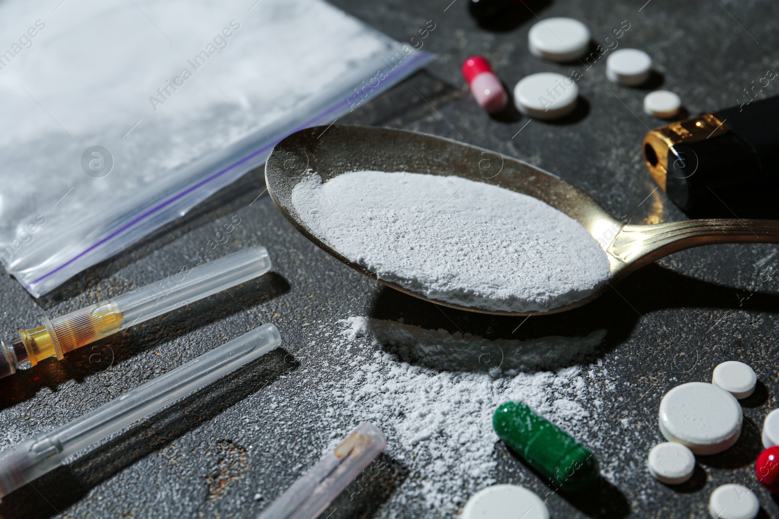 Photo of Drug addiction. Plastic bag with powder, spoon, and syringes on gray textured table, closeup