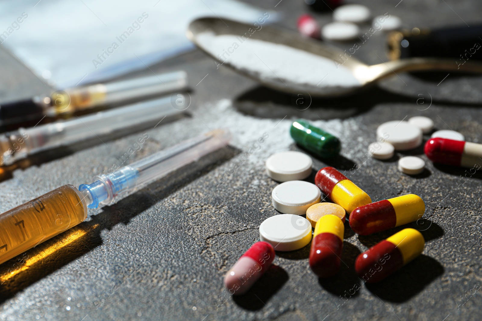 Photo of Drug addiction. Different pills, syringes and spoon with powder on gray textured table, closeup