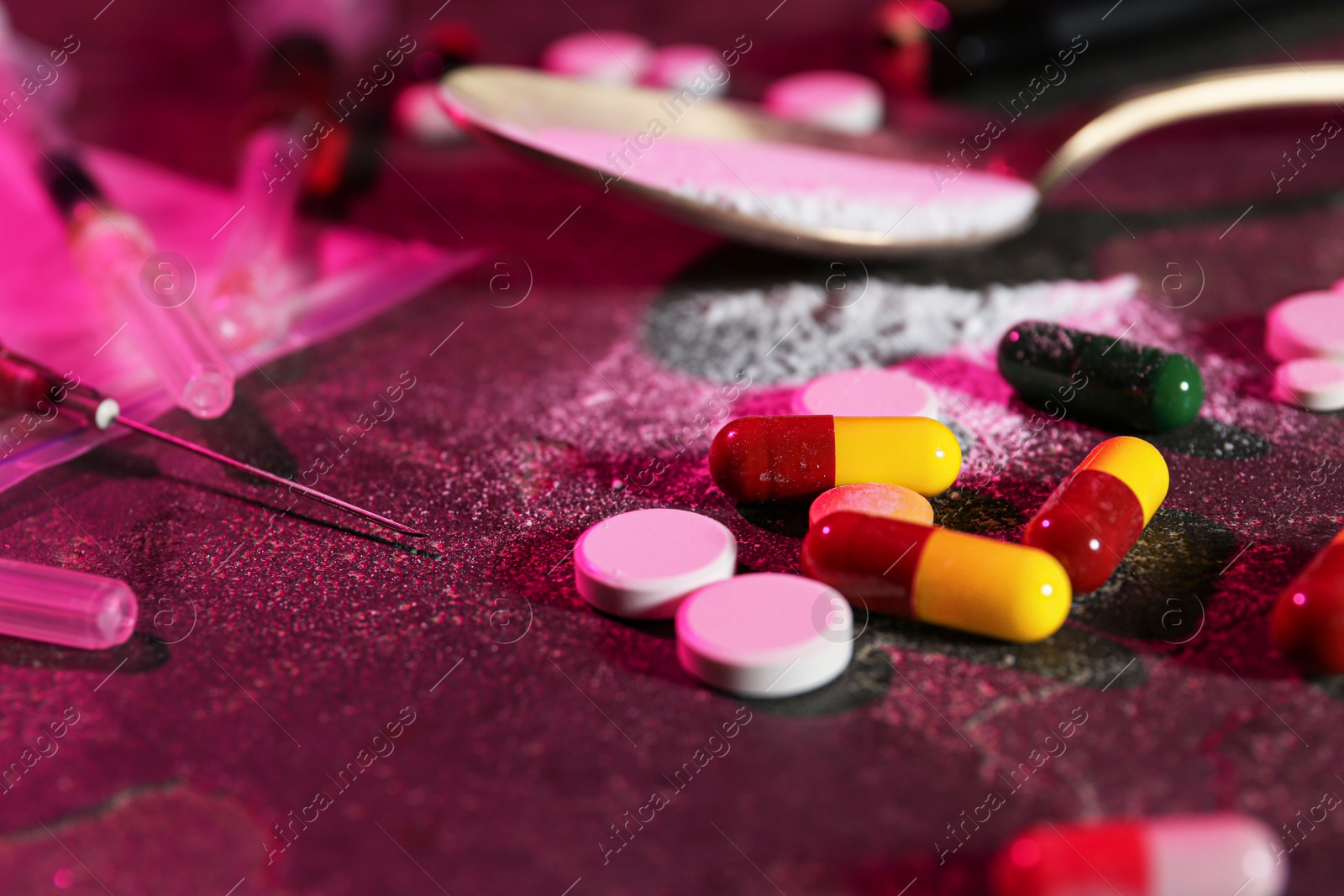 Photo of Drug addiction. Different pills, powder and syringes on dark table in color light, closeup