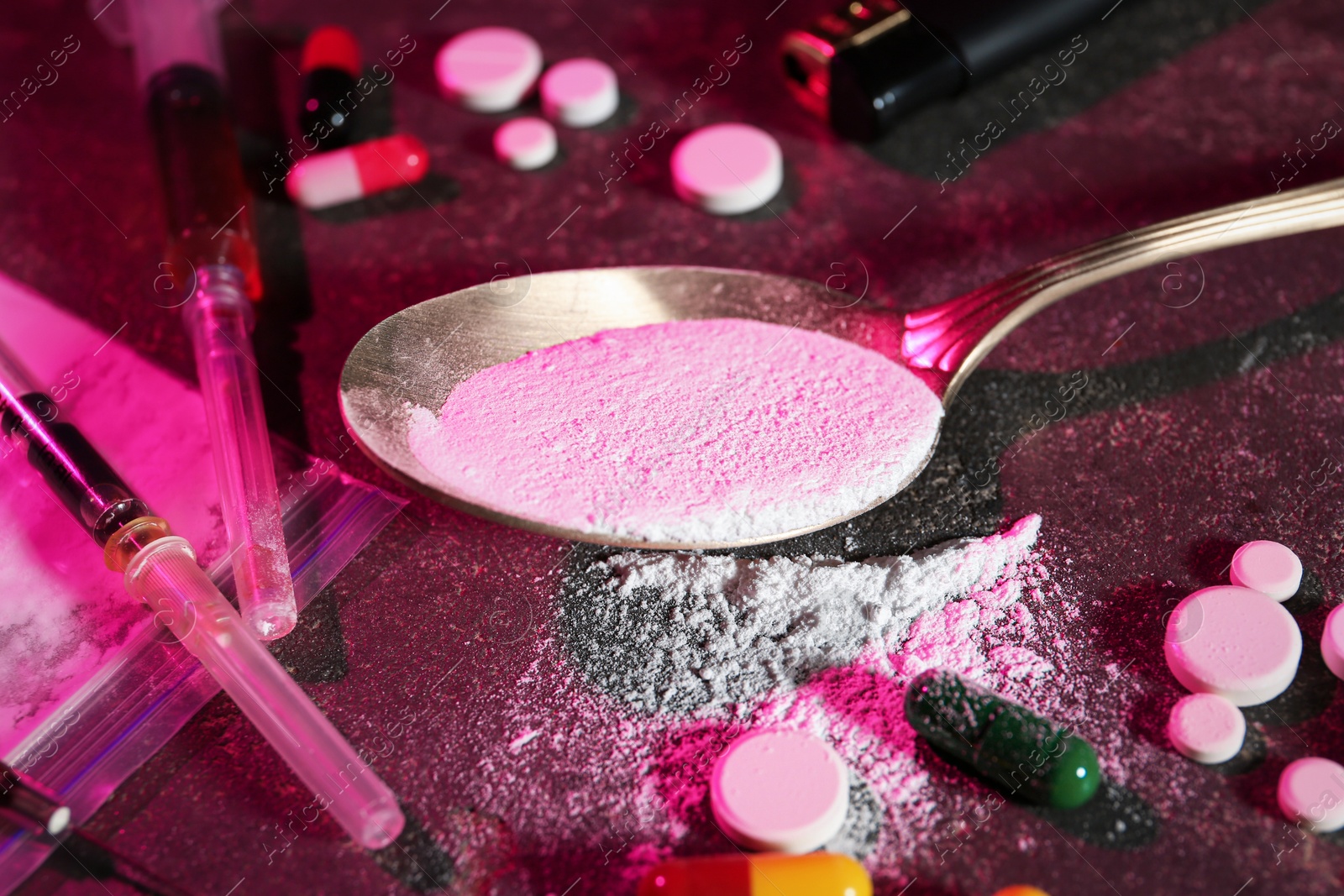 Photo of Drug addiction. Spoon with powder, different pills and syringes on dark table in color light, closeup