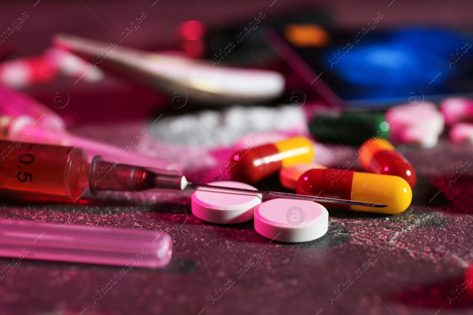 Photo of Drug addiction. Different pills and syringes on dark table in color light, closeup