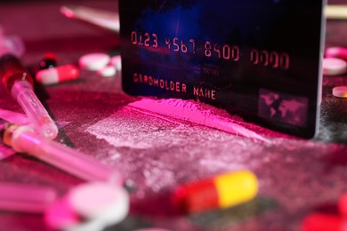 Photo of Drug addiction. Credit card, powder, pills and syringes on dark table in color light, closeup