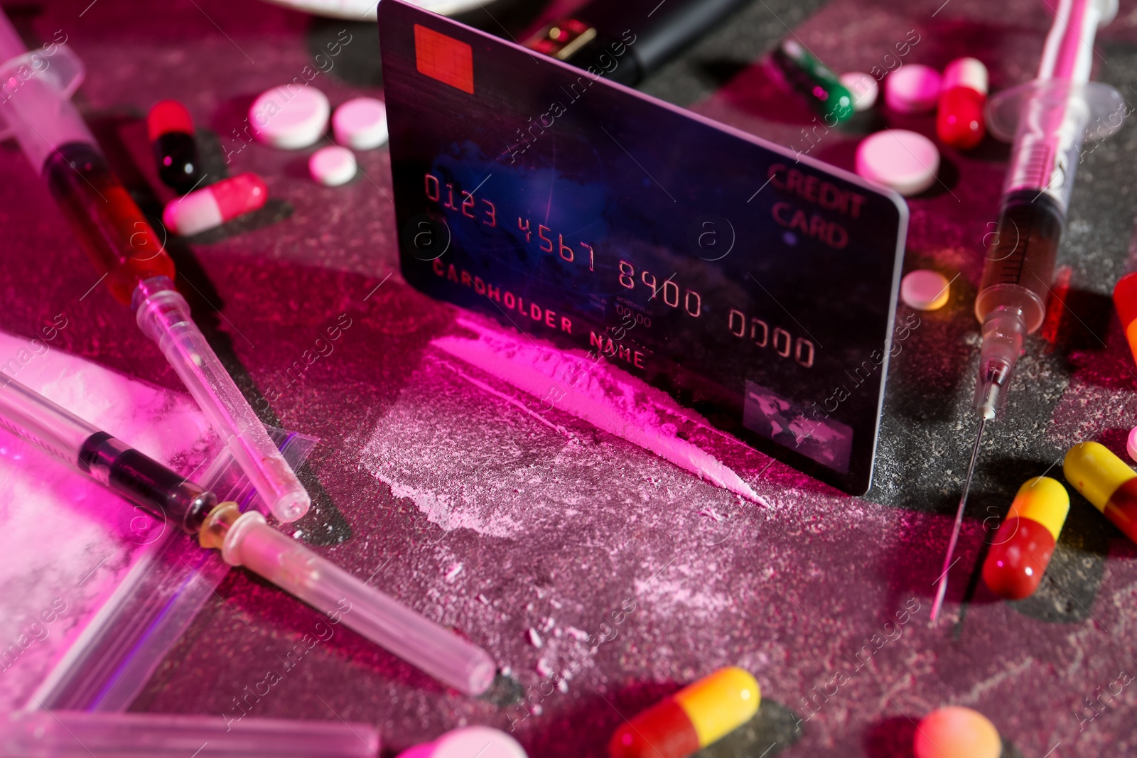 Photo of Drug addiction. Credit card, powder, pills and syringes on dark table in color light, closeup