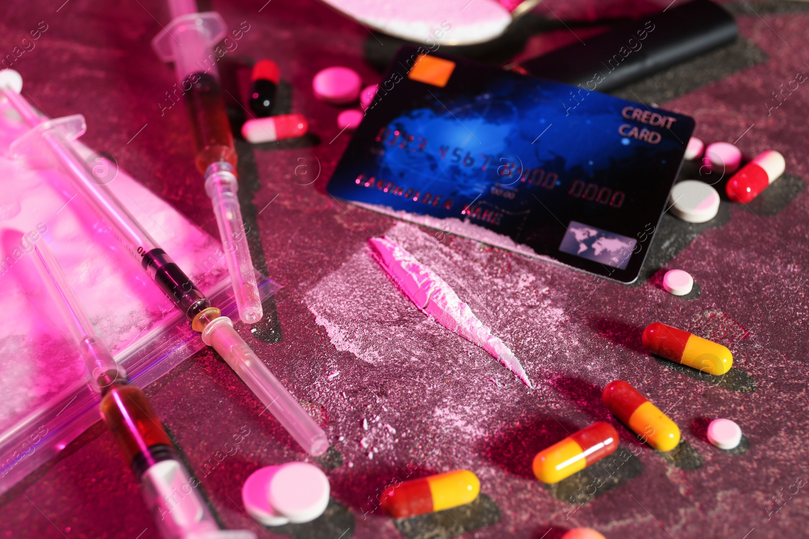 Photo of Drug addiction. Plastic bag with powder, credit card, pills and syringes on dark textured table in color light, closeup