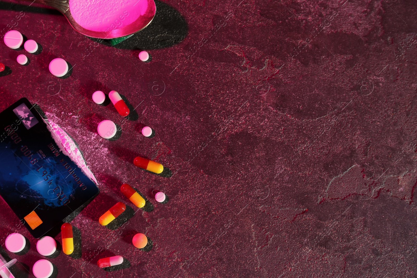 Photo of Drug addiction. Spoon with powder, credit card and pills on dark textured table in color light, flat lay. Space for text