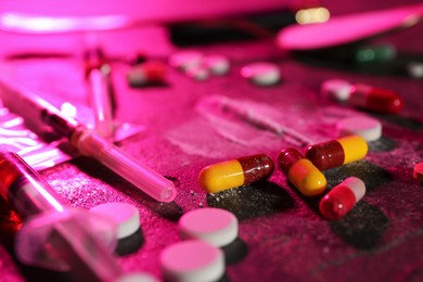 Photo of Drug addiction. Different pills and syringes on table in color light, closeup