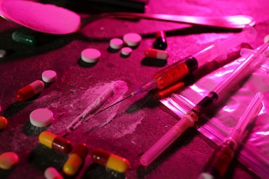 Photo of Drug addiction. Plastic bag with powder, syringes and pills on table in color light, closeup