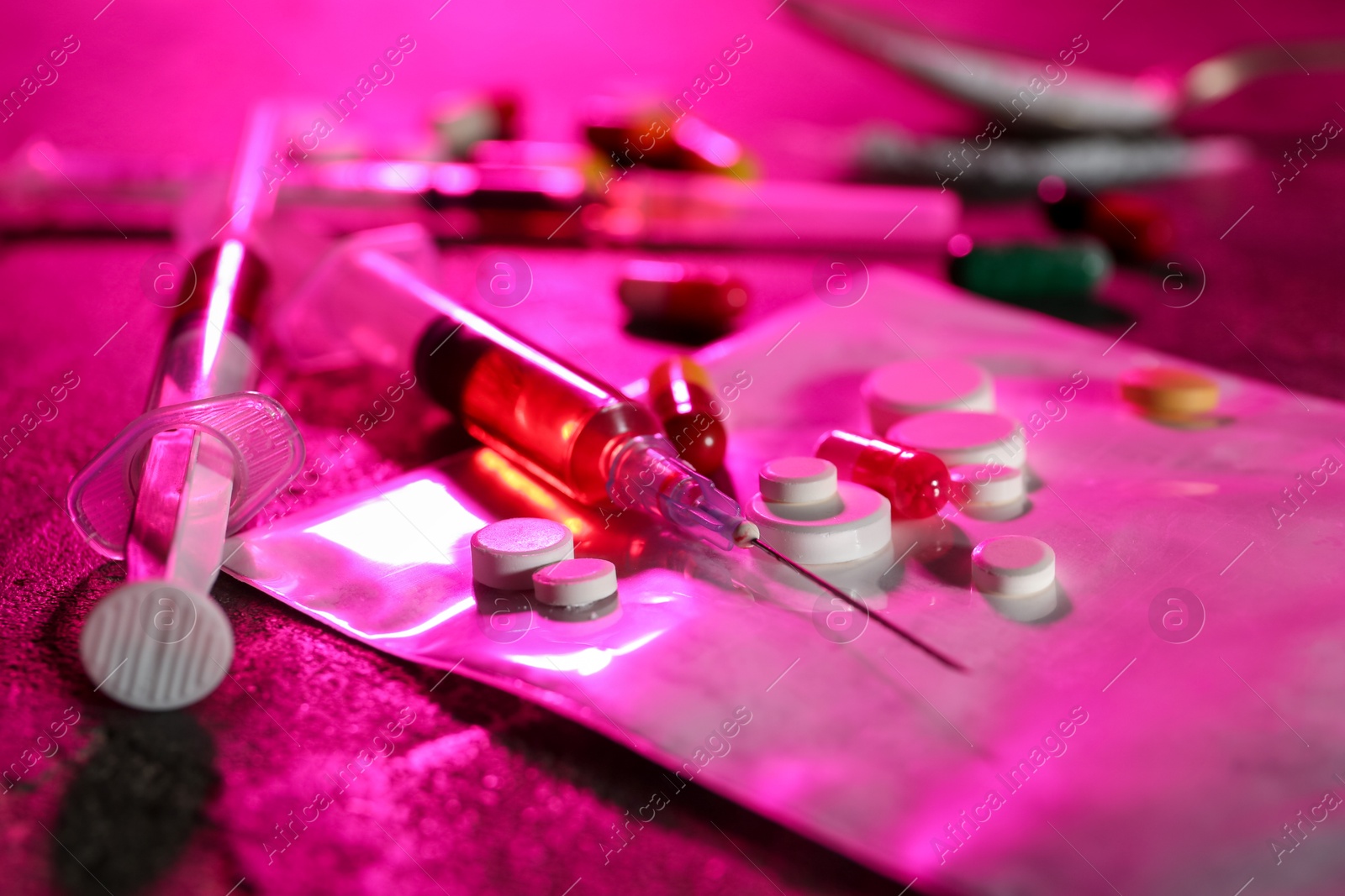 Photo of Drug addiction. Plastic bag with powder, syringes and pills on table in color light, closeup