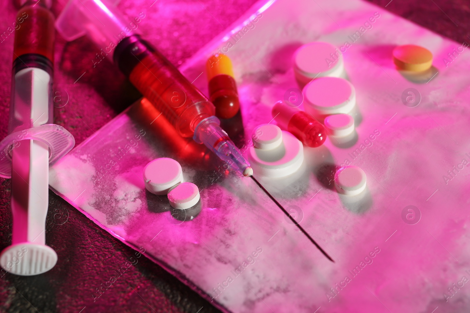 Photo of Drug addiction. Plastic bag with powder, syringes and pills on table in color light, closeup