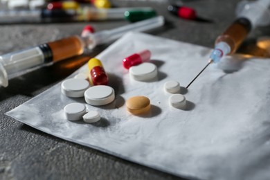 Photo of Drug addiction. Plastic bag with powder, syringes and pills on gray textured table, closeup