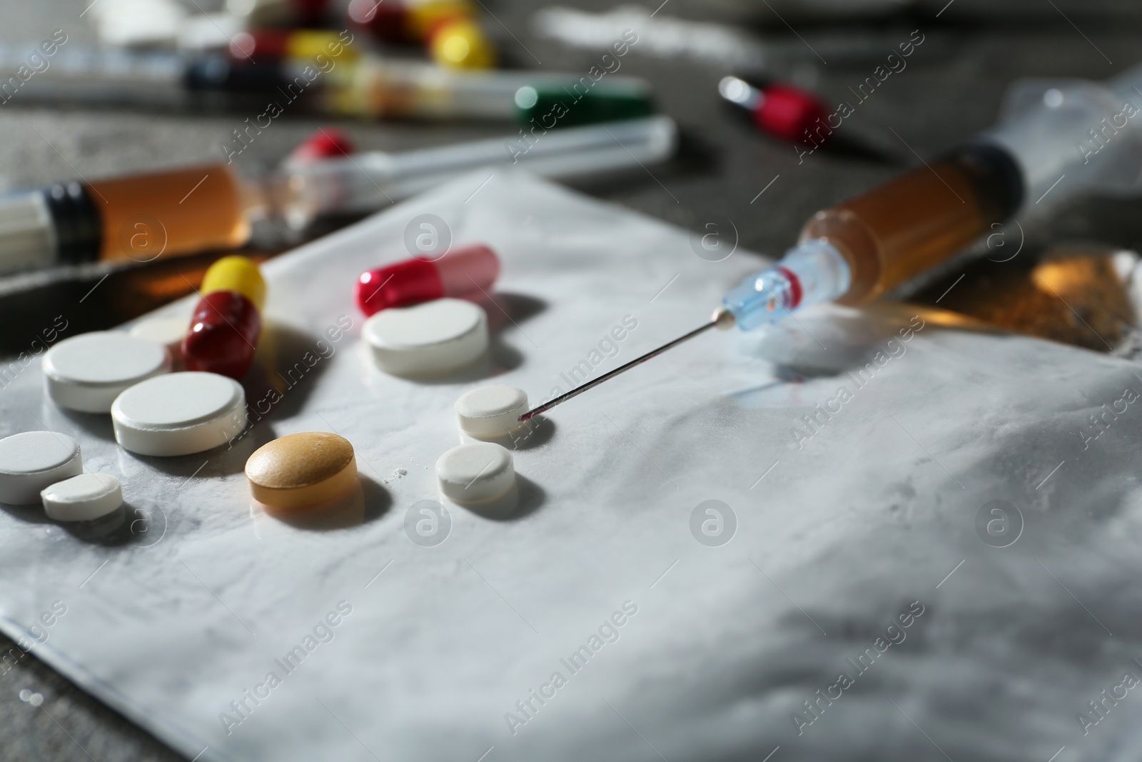 Photo of Drug addiction. Plastic bag with powder, syringes and pills on gray table, closeup