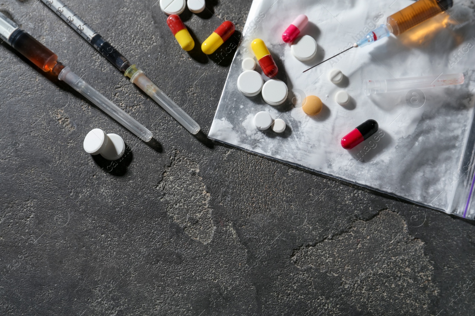 Photo of Drug addiction. Plastic bag with powder, syringes and pills on gray textured table, flat lay. Space for text