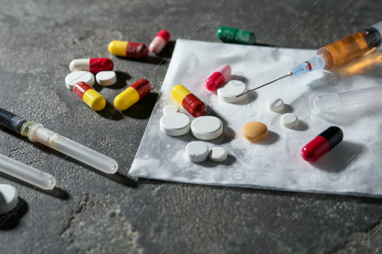 Photo of Drug addiction. Plastic bag with powder, syringes and pills on gray textured table, closeup