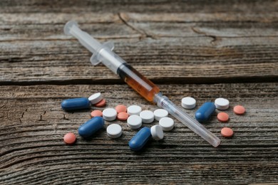 Photo of Drug addiction. Syringe and pills on wooden table