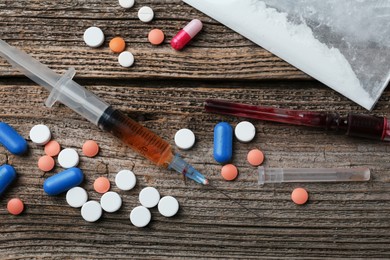 Photo of Drug addiction. Plastic bag with powder, syringes and pills on wooden table, flat lay