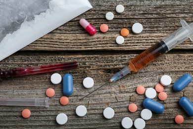 Photo of Drug addiction. Plastic bag with powder, syringes and pills on wooden table, flat lay